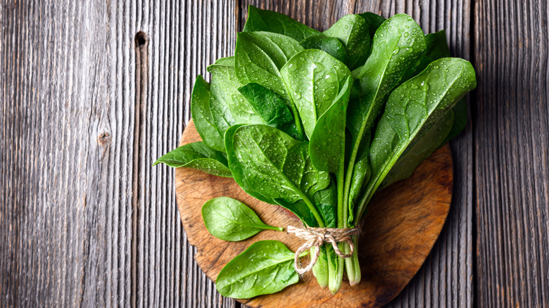 A bundle of fresh spinach on a round wooden plate