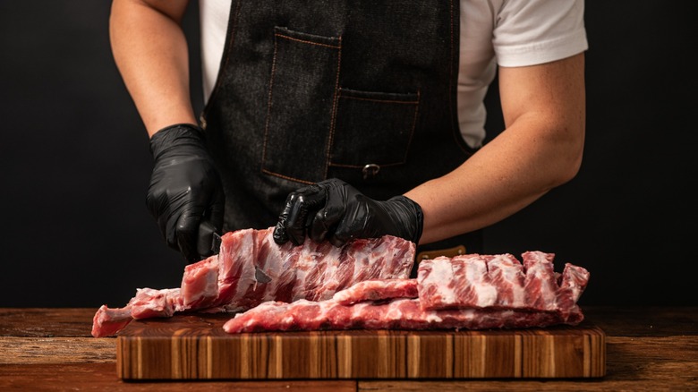 person with gloves and apron preparing ribs