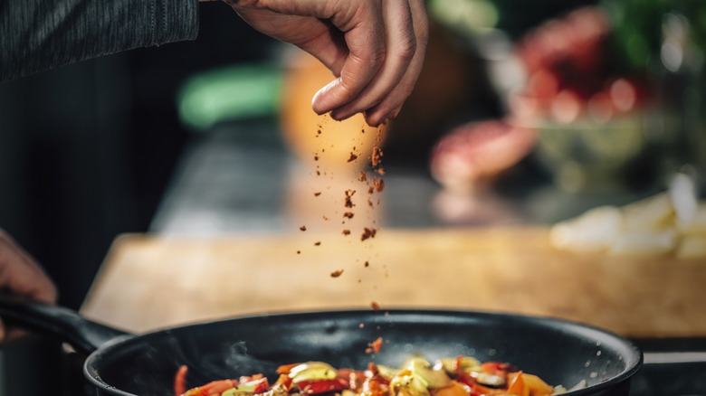 a hand sprinkles seasoning on a saute pan