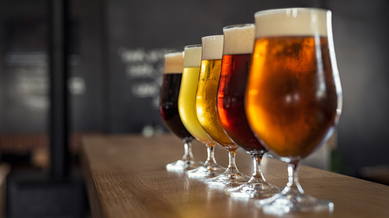Tulip-shaped glasses with different varieties of beer on wooden bar.