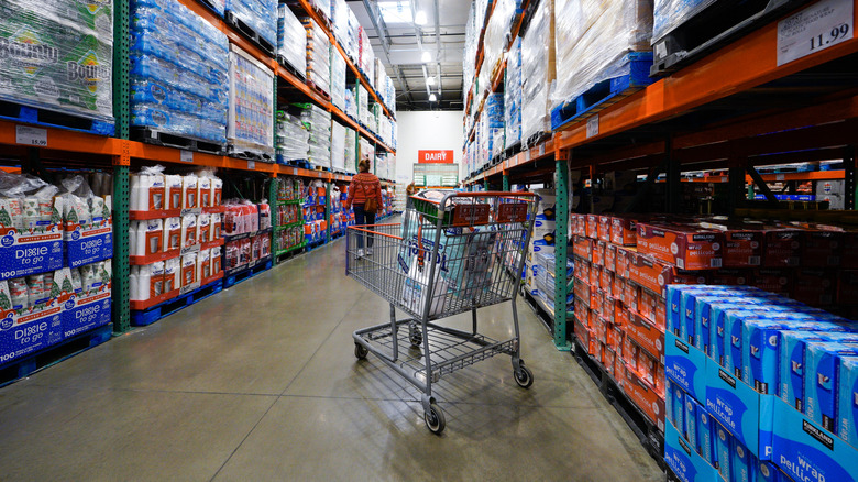 Interior of Costco warehouse aisle with cart and shopper.