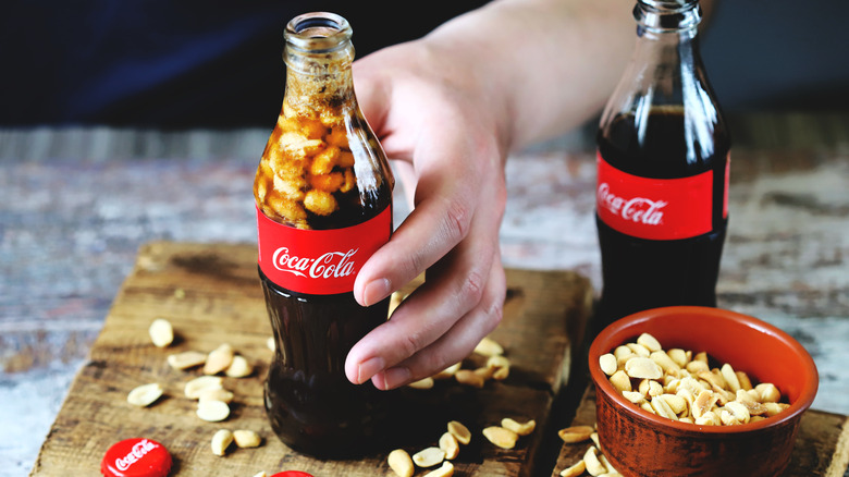 Hand holding a bottle of Coca Cola with peanuts