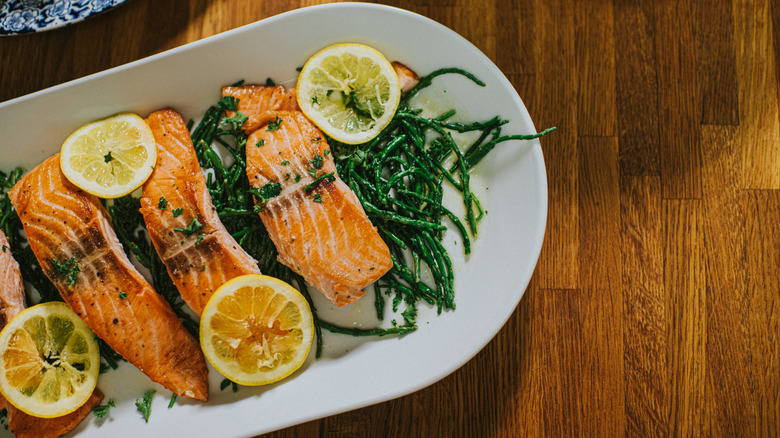Four cuts of cooked salmon garnished with lemon and herbs on a white plate