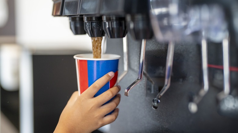 hand fills a paper cup from a fast food soda machine