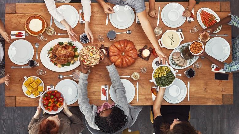 Overhead view of hands passing dishes over a holiday table.