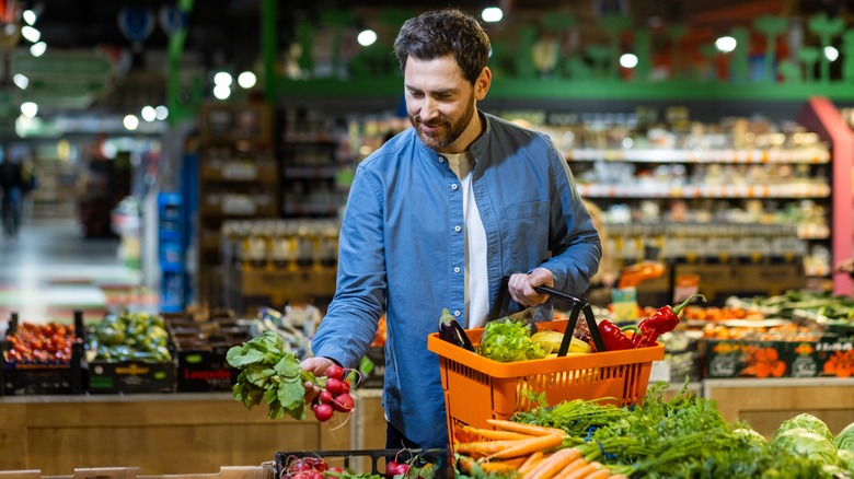 A shot of a man picking out fresh produce at a supermarket, with an orange basket of produce in his hand