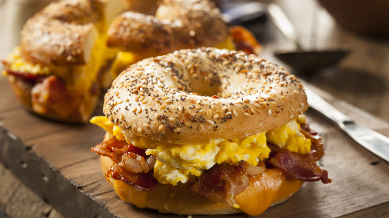 A close-up of an egg, cheese, and bacon sandwich on an everything bagel, with another cut in half in the background