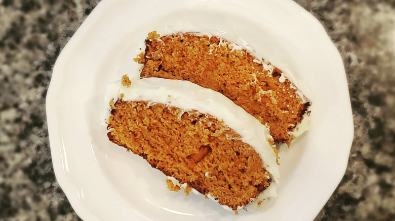 Slice of tomato soup cake and white frosting on white plate, overhead view