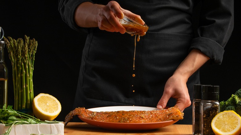 Chef pouring marinade over fish in white bowl.