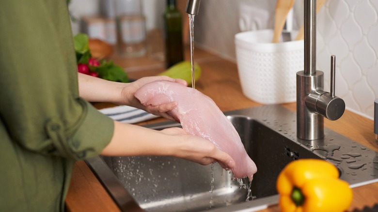 woman washing a large chicken breast under the stream of a kitchen faucet