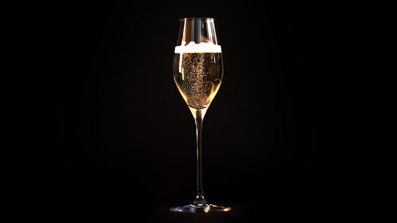 Champagne or sparkling wine in glass isolated against black background.
