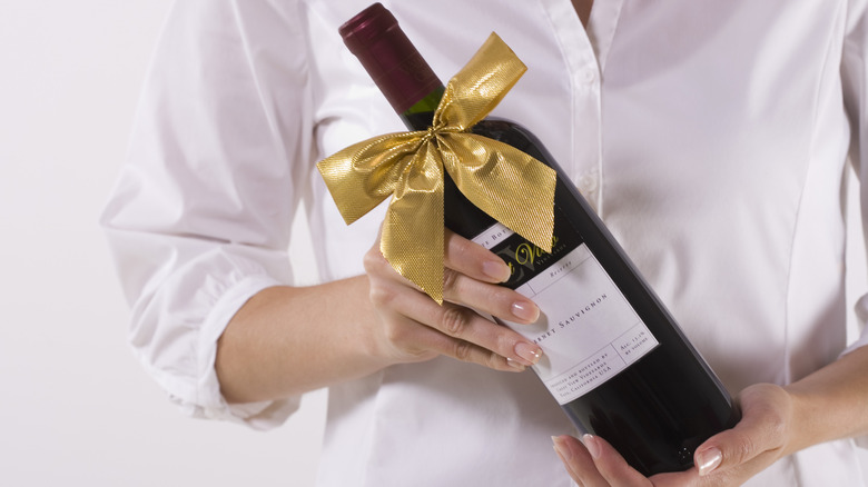Hands holding a bottle of wine with a gold bow.