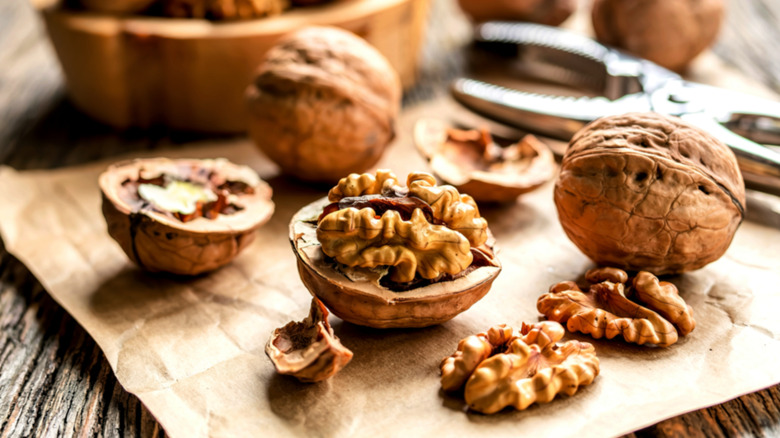 Several whole and shelled walnuts on a wooden cutting board along with a nutcracker