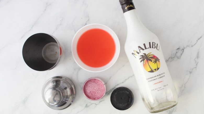 Malibu bottle next to pink liquid in bowl and cocktail shaker