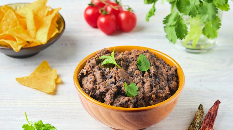 Refried beans in a bowl with tortilla chips, tomatoes, cilantro, and chili peppers