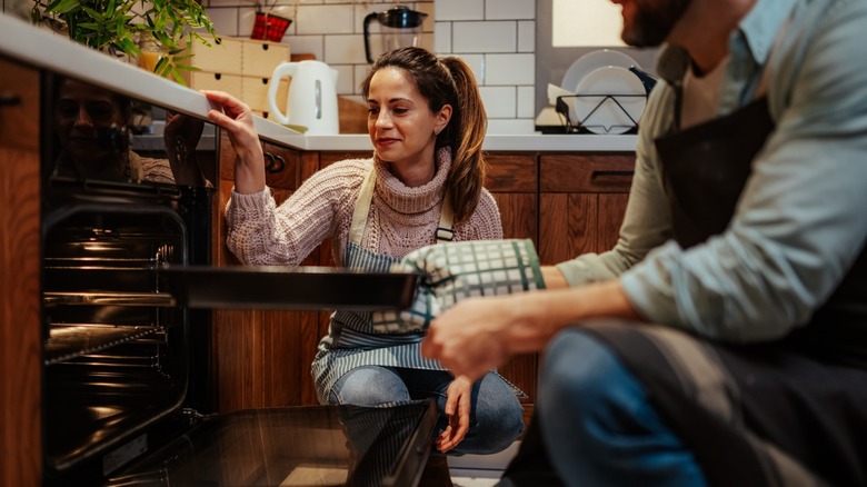 couple puts food in oven together