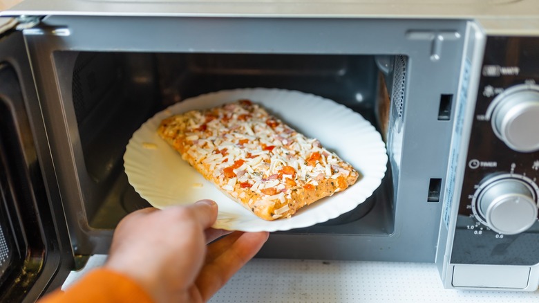 Someone putting a rectangular frozen pizza in the microwave