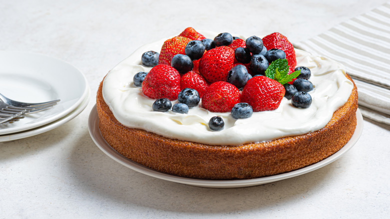 A fresh sponge cake topped with white icing, strawberries, and blueberries