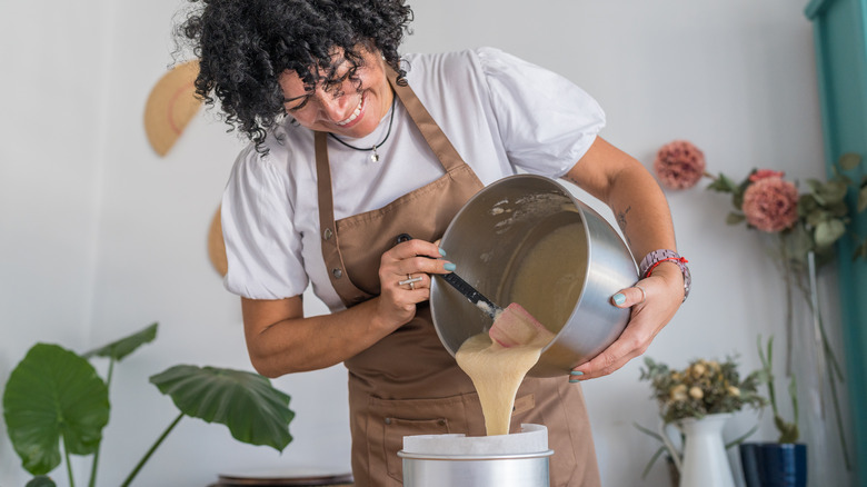Smiling person pouring cake batter from a mixing bowl into pan.