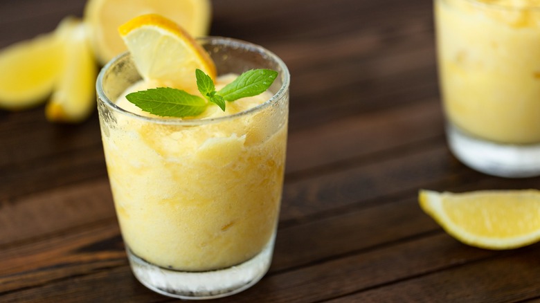 Lemon slushy drink with lemon wedge and mint sprig as garnish