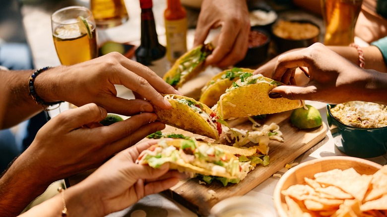 Closeup of hands holding tacos over restaurant table.