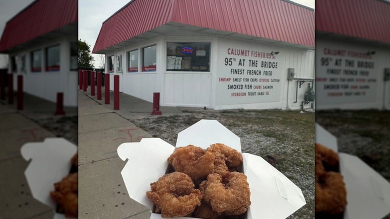 Someone holding a box of breaded fish in front of Chicago's iconic Calumet Fisheries