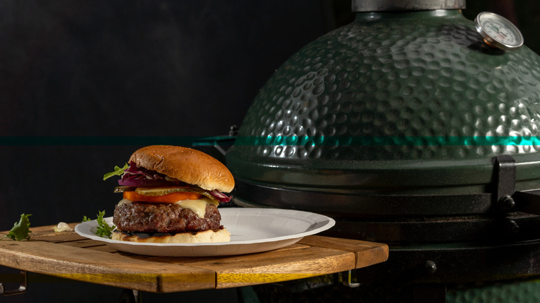 A home made burger next to an egg-type grill