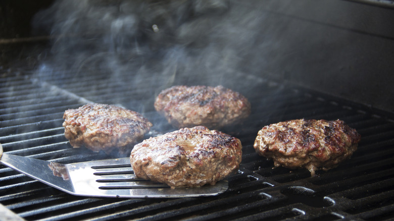 Four hamburgers cooking on a barbeque grill