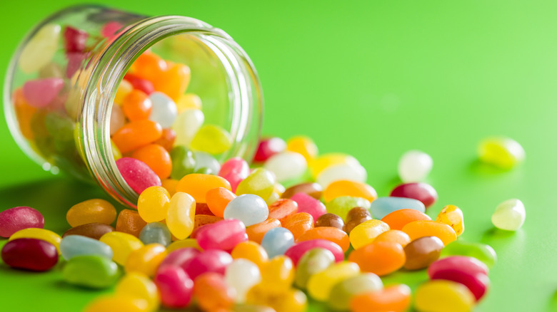 Multicolored jelly beans spilling out of a glass jar onto a bright green background