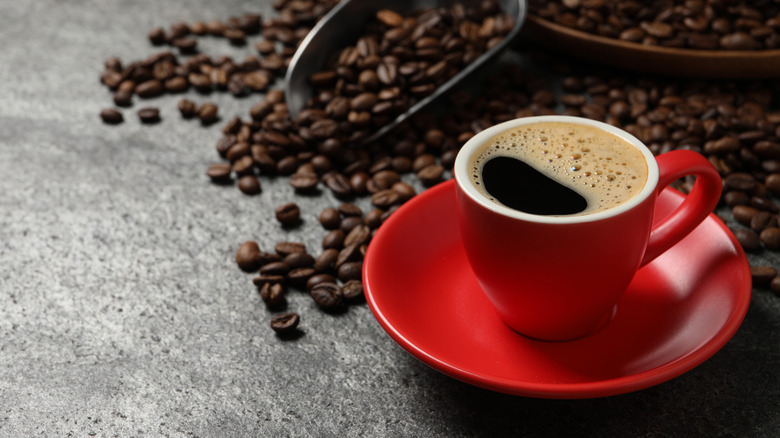 Coffee in a red cup with coffee beans and a gray backdrop