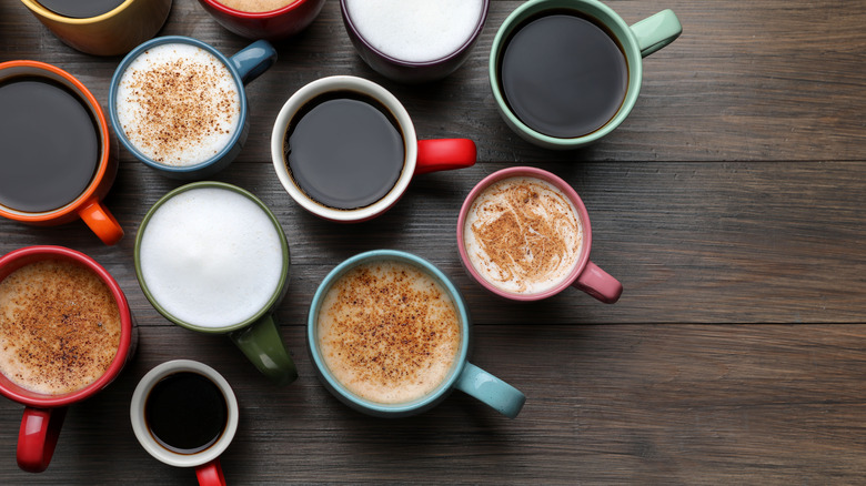 Different coffees in various colored cups on wooden surface