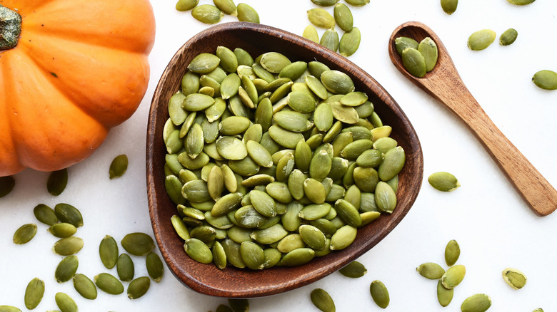 Pumpkin seeds in a wooden bowl next to a spoon